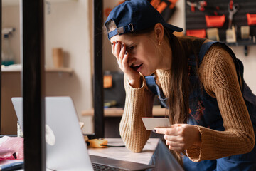 Anxious female repair shop owner facing online fraud issues while holding business credit card