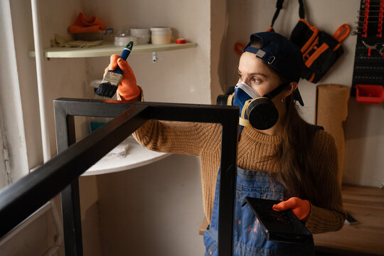 Female repair worker painting black paint metal table legs in small workshop or garage - Powered by Adobe