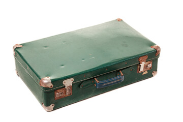 A green suitcase sits on a plain surface, showing signs of age with dents and worn metal edges. This vintage item features a sturdy handle and is likely used for travel or as decor