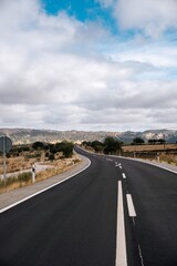 Fototapeta premium Empty rural road winding through the dry Iberian scrubland under a cloudy sky, Cáceres, Spain.