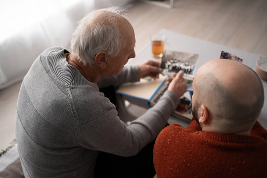 Elderly father and son looking at old photo album recalling shared family memories together - Powered by Adobe
