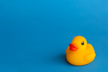 Yellow rubber duck isolated on a bright blue background, positioned in the bottom right corner, slightly elevated angle. Concept of childhood, fun, nostalgia, simplicity, minimalism, hygiene