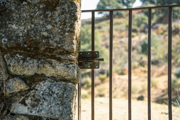Close-up of a rusted metal bolt and latch on an open iron gate attached to an ancient stone column, Cáceres, Spain.