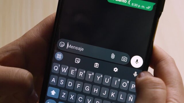 Close-up view of someone holding a smartphone and typing the message &ldquo;Lo siento :(&rdquo; on a dark-themed keyboard, with their thumbs positioned over the screen while composing a text.