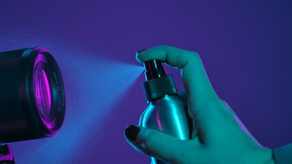 Close Up of Hand with Spray Bottle and Camera Lens under Neon Light