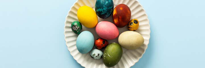 Beautifully decorated Easter eggs in vibrant colors are displayed on a white plate against a light blue background, symbolizing the joy of Easter festivities, banner