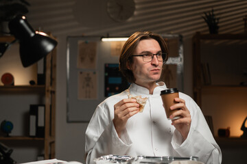 Overworked doctor drinking takeaway coffee and eating takeout meal at desk during long night shift