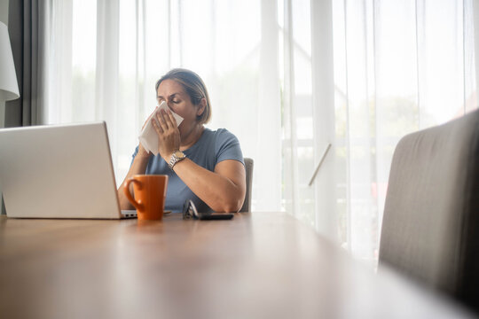 Woman blowing her nose with tissue while working from home on laptop