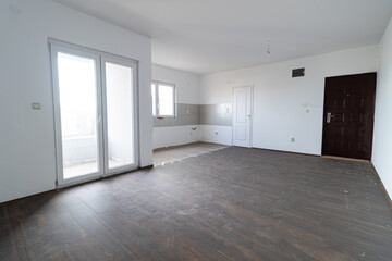 Fototapeta premium Empty apartment room with white walls and a dirty wood laminate floor. Empty apartment room. Room apartment under renovation