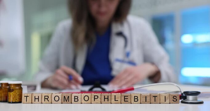 Miniature wooden cubes on table form word Thrombophlebitis. Woman doctor writes medical instructions with great accuracy on patient treatment form