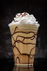 Vanilla milkshake with chocolate syrup in clear glass on dark background.