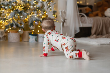 A one-year-old baby crawls on all fours, dressed in a New Year's outfit, crawling around a New Year's-decorated room, smiling. New Year and Christmas. Parenting. Family