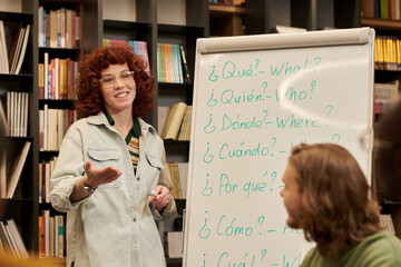 Young woman teaching language lesson, standing near flip chart with Spanish and English question...