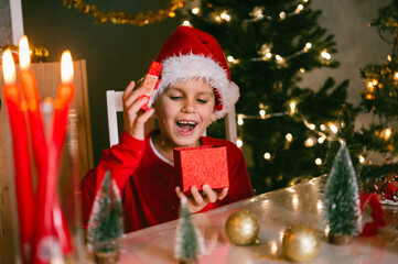 Merry Christmas and happy holidays. A cheerful funny boy 7 y.o. with a gift. A child is having fun near a tree.