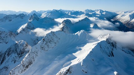 Aerial view of majestic snowcovered mountain range peaks piercing through lowlying clouds under a clear blue sky during winter