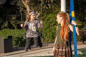 Mother and daughter smiling at each other while playing on a swing set in a park.