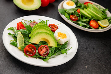 Avocado salad arugula, egg, tomato, mixed greens, vegetables dish fresh delicious gourmet food background tabletop rustic food top view copy space keto and paleo diet vegetarian food