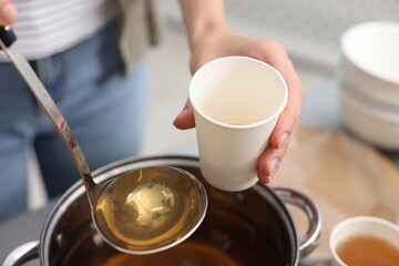 Homeless shelter. Volunteer pouring drink into cup at table indoors, closeup