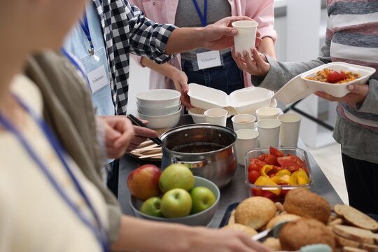 Volunteers giving food to homeless people in shelter, closeup