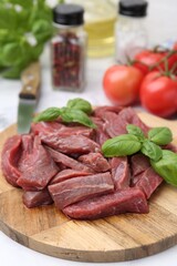 Pieces of raw beef meat, basil and ingredients on table, closeup