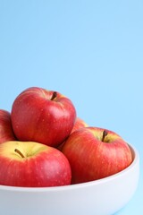 Ripe red apples in bowl on light blue background, closeup. Space for text
