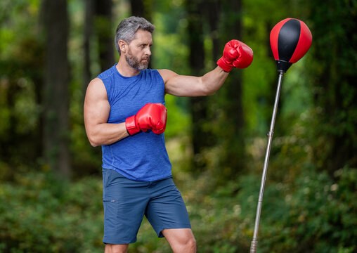 Strong athlete man boxer. Boxer in sportswear. Exercising and punching. Punching bag workout. Sportsman boxing freestanding punching bag outdoor. Sport man boxing punching bag