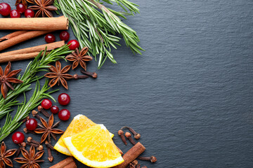 Different spices, fresh rosemary, cranberries and orange slices for mulled wine on black table, top view. Space for text