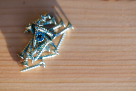 Top view of scattered screws on a wooden board, one star-shaped head in sharp focus, concept of choice, focus and construction projects.