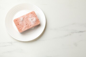 Kitchen sponge with foam and plate on white marble table, top view. Space for text