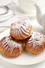 Tasty profiteroles with powdered sugar served on white table