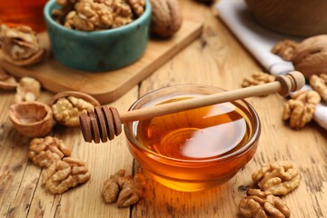 Delicious honey in glass bowl, dipper and walnuts on wooden table, closeup