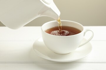 Pouring hot tea into cup from teapot at white wooden table, closeup