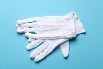 Pair of white cloth gloves on light blue background, top view