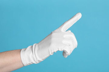 Woman in cloth glove pointing at something on light blue background, closeup. Space for text