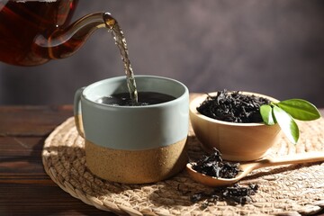 Pouring hot tea into cup from teapot at wooden table, closeup