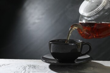 Pouring hot tea into cup from teapot at grey table, closeup. Space for text