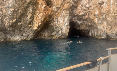 Swimmers explore the crystal-clear turquoise waters near Montenegro's dramatic Blue Cave, carved into towering limestone cliffs.
