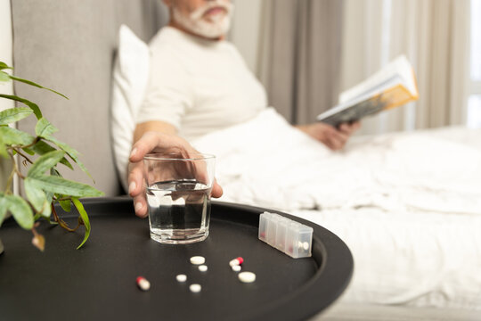 Senior man taking medication with water while reading in a cozy room
