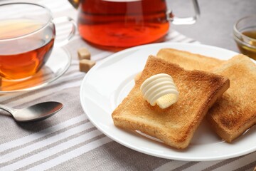 Fresh toasted bread slices with butter and tea on table, closeup