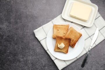 Fresh toasted bread slices with butter on grey table, flat lay. Space for text