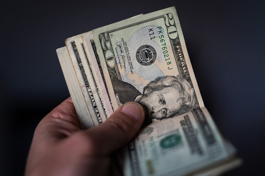 A hand holds a stack of US currency, with a twenty-dollar bill visible on top. Financial concept of earning, spending, budget, or saving money.