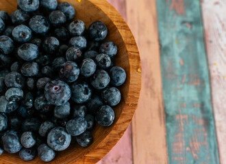 A close-up view of fresh blueberries resting in a wooden bowl on a distressed pastel table surface. Ideal for culinary blogs, healthy eating, product packaging, and natural food concepts.