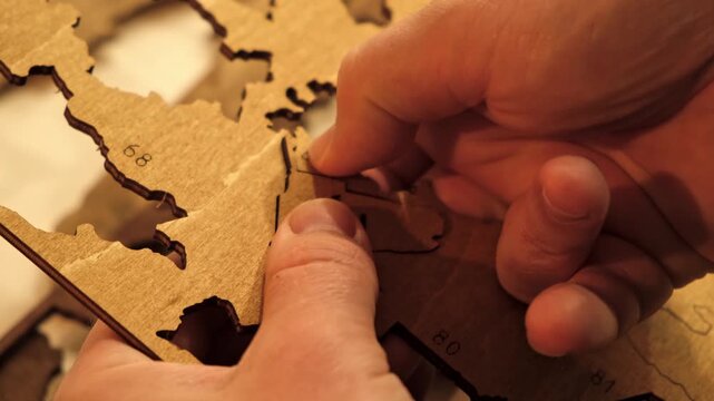 Male hands take out a laser-cut piece from a sheet of plywood to assemble a decorative wooden world map. The creative process of creating DIY crafts. Hobby concept. Carpentry. High quality 4K footage.