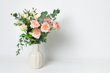Elegant arrangement of soft pink roses and greenery in a textured ceramic vase, showcasing a fresh...