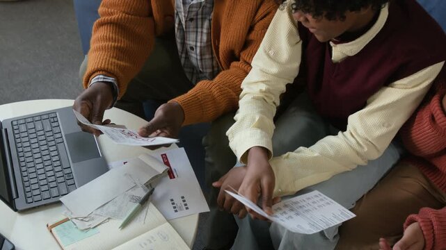 High angle shot of African American grandfather holding past due invoice while grandsons helping sort through household bills sitting at tea table with open laptop in living room