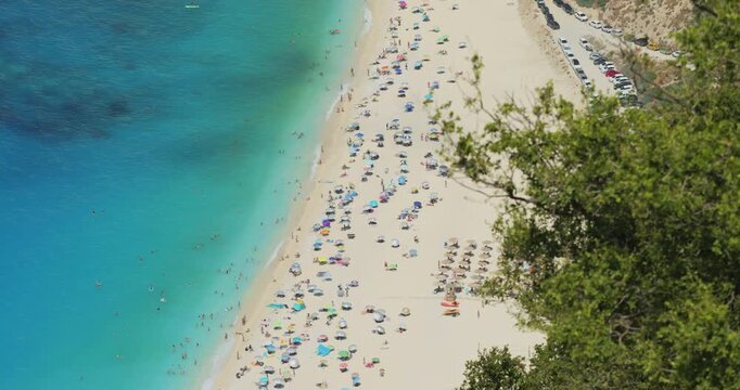Breathtaking top view of Mediterranean turquoise sea and Myrtos white beach framed by green mastic shrub branches waving in summer breeze, Kefalonia island, Greece