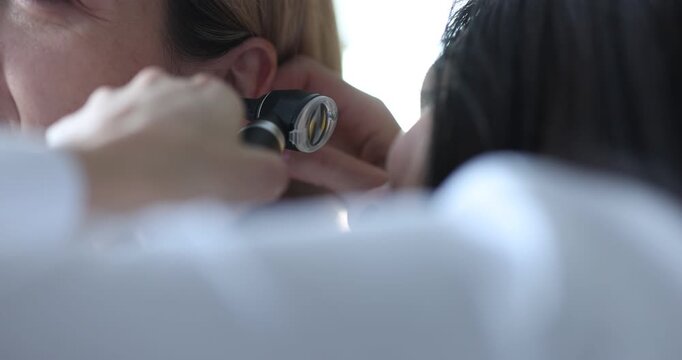 Doctor holds otoscope near patient ear during careful examination. Specialist checks ear canal as looking for infection and wax plug at appointment