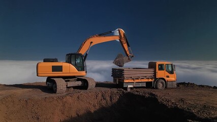 An excavator loads soil and rocks into a waiting dump truck at a construction or mining site. Heavy machinery in action highlights industry, labor, and large-scale earthmoving operations. - Powered by Adobe