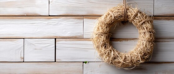 Rustic wreath of natural twigs and hay hangs on weathered white wooden wall showcasing cozy holiday vibes