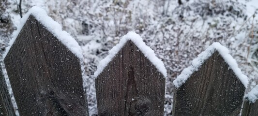 Snow covers wooden fence peaks in a quiet winter landscape by a field